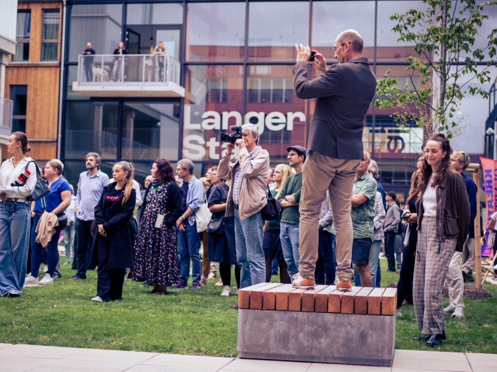 Besucher fotografiert von einem Sockel aus über die Menge hinweg vor der Fassade „Langer Stall“