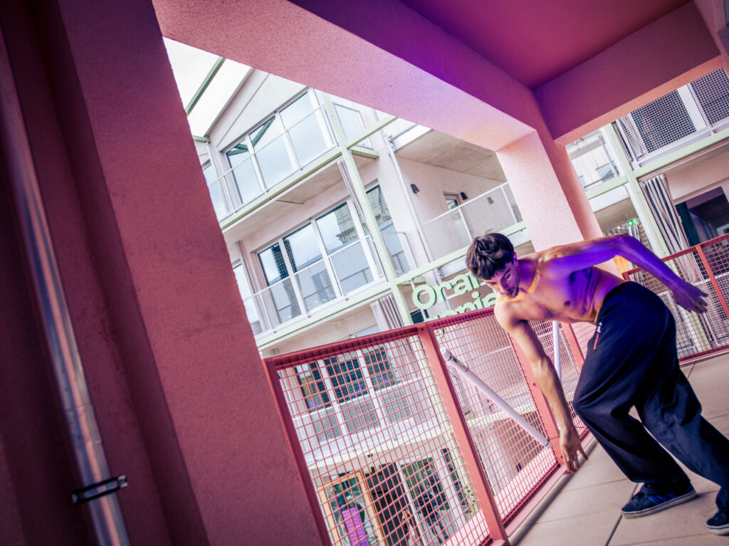 Oberkörperfreier Tänzer in dynamischer Pose auf einem Balkon der „Akademie“
