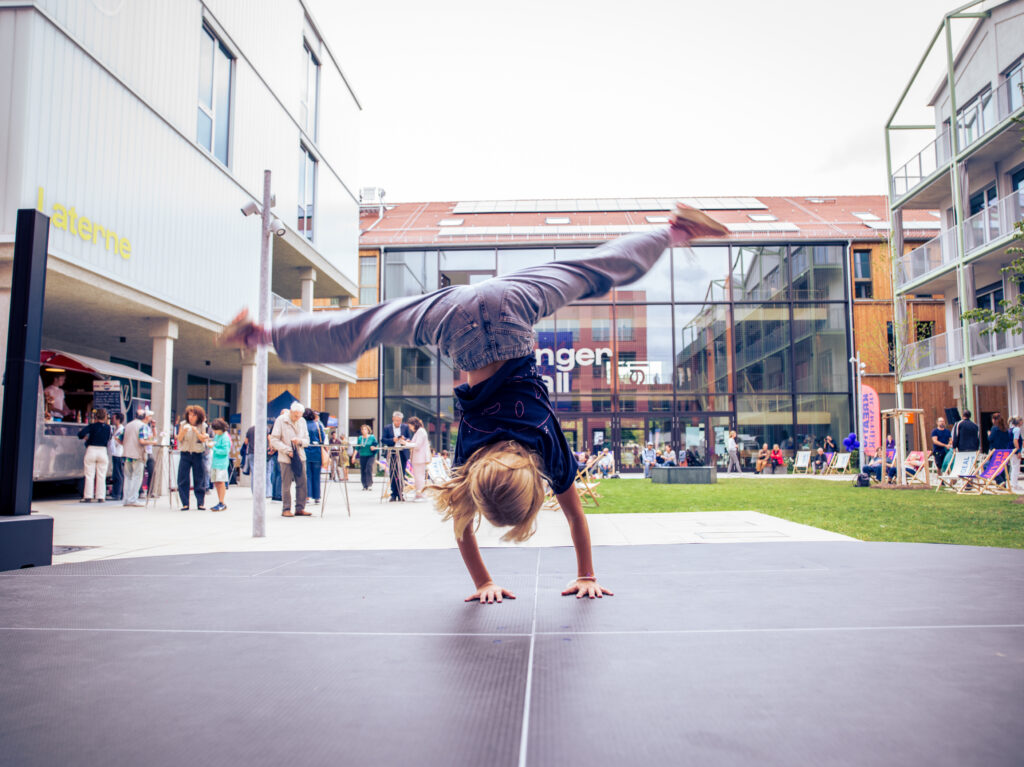 Person macht einen einhändigen Handstand auf dem Platz vor der Fassade „Langer Stall“