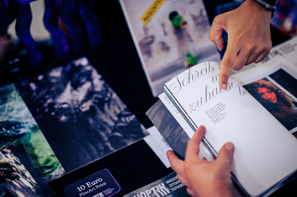 Hände blättern in einem Fotoheft mit Kalligrafie-Schriftzug an einem Stand für Fine-Art-Prints