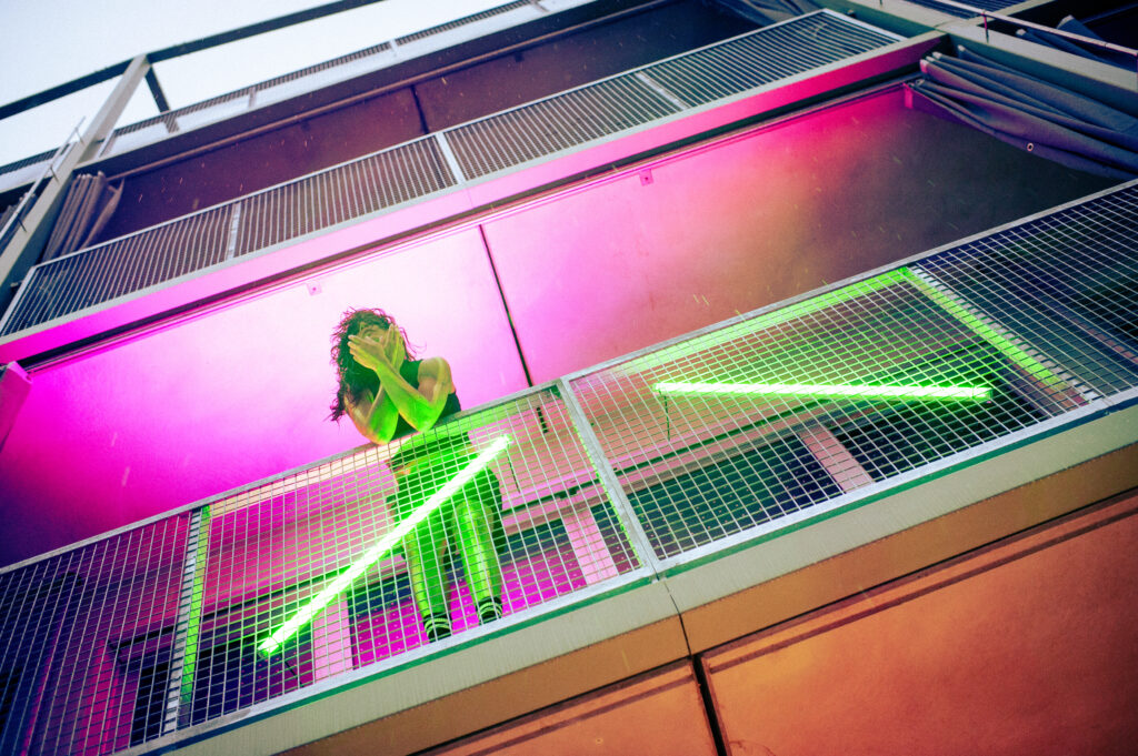 Person auf einem Balkon im pink-grünen Neonlicht einer Lichtinstallation