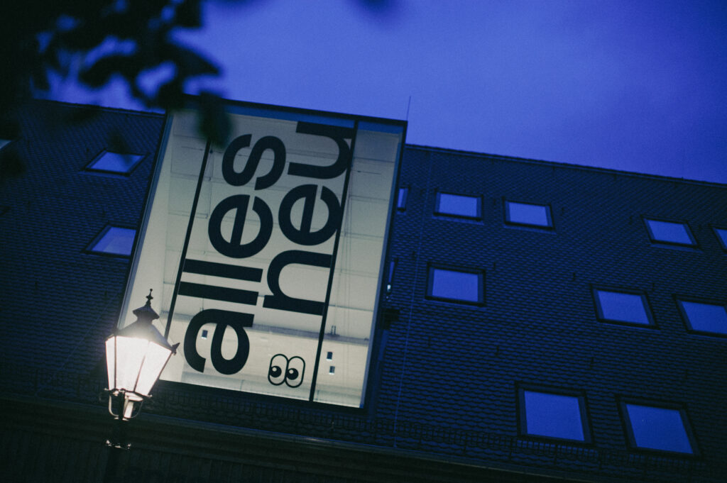 Gebäude mit Leuchtschrift „Alles neu“ in der Abenddämmerung, davor eine Straßenlaterne